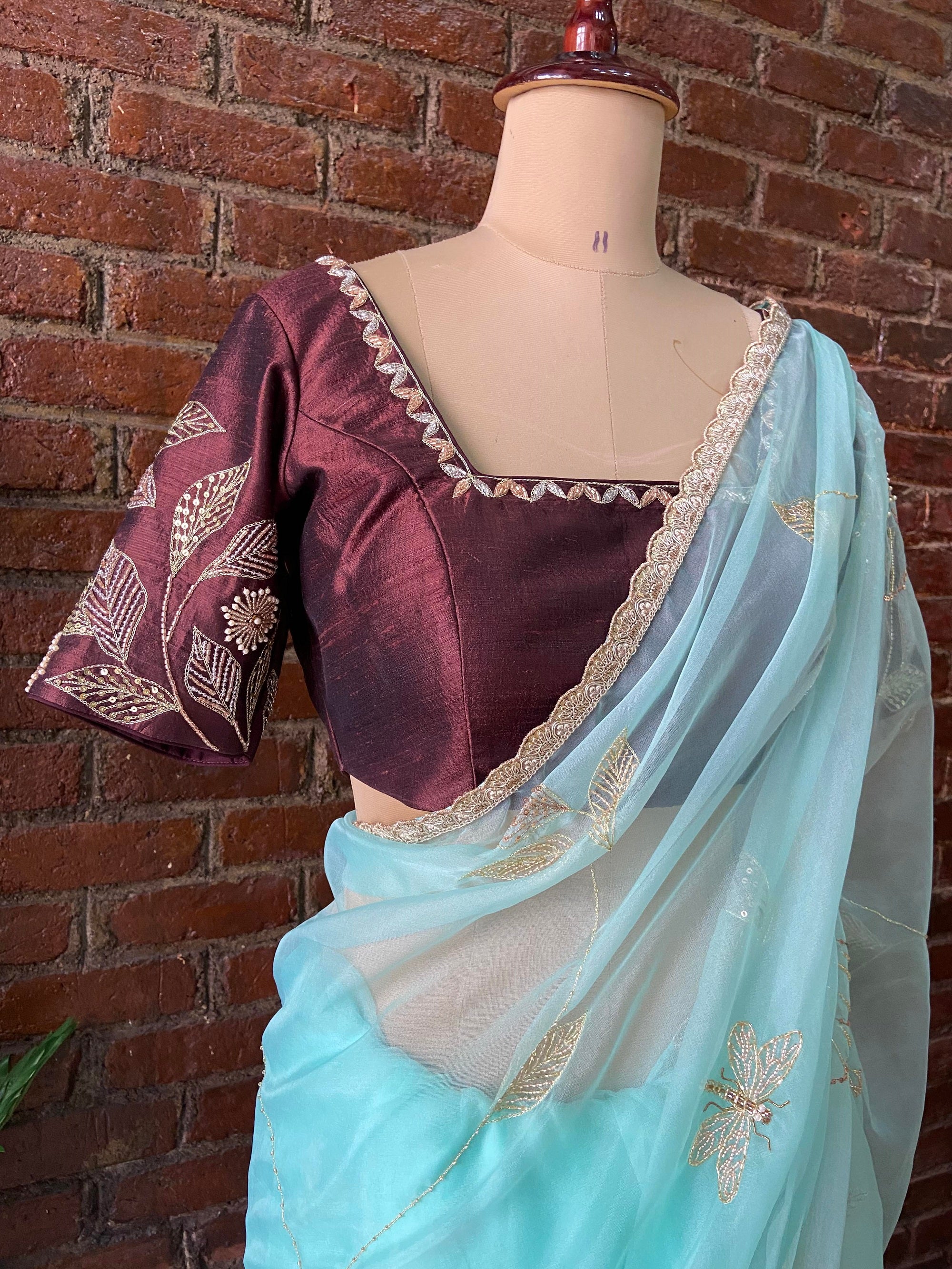 Ice Blue Organza Embroidered Saree -  A maroon blouse with gold embroidery and a light blue saree